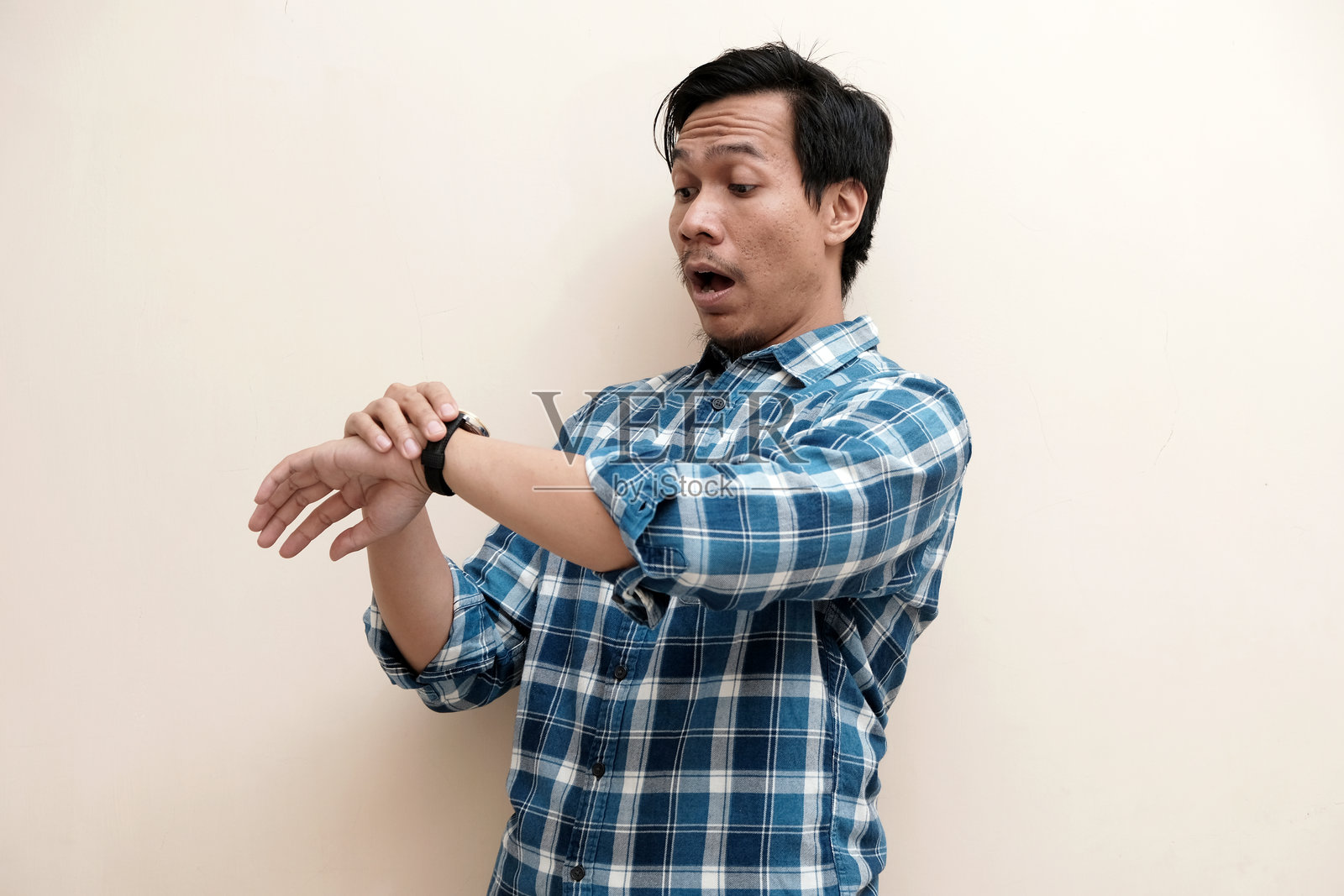 东南亚男子穿着格子衬衫，拿着手表，表情震惊照片摄影图片