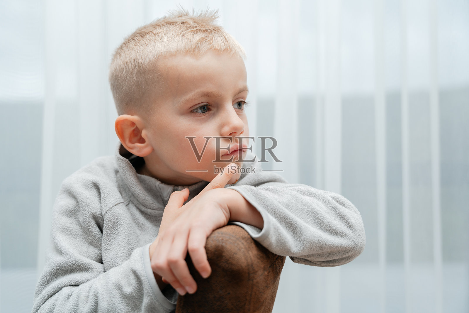 柔和的光线下，一个孩子带着若有所思的表情坐着，中性色调和放松的姿势营造出亲密的肖像。照片摄影图片