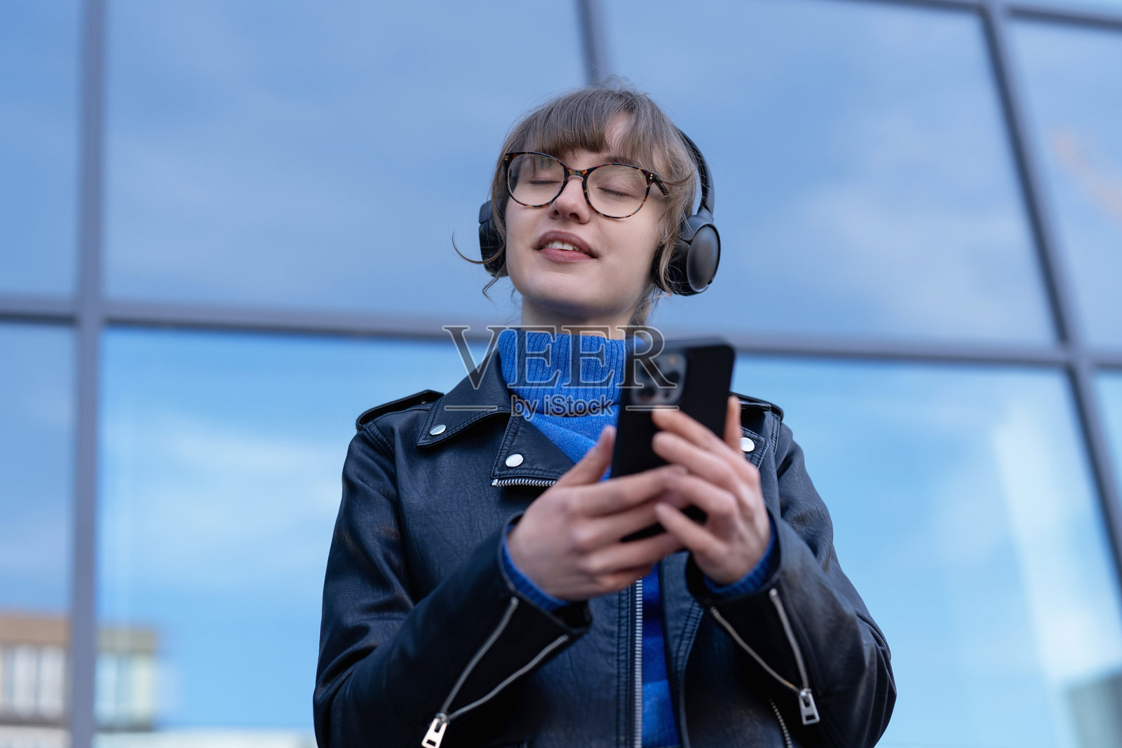 年轻人在现代玻璃建筑附近使用智能手机享受音乐照片摄影图片