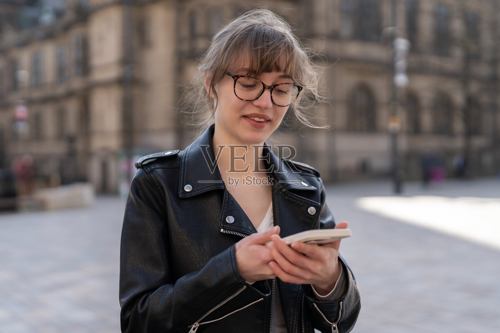 年轻女子白天在历史建筑附近的城市广场上使用智能手机照片摄影图片