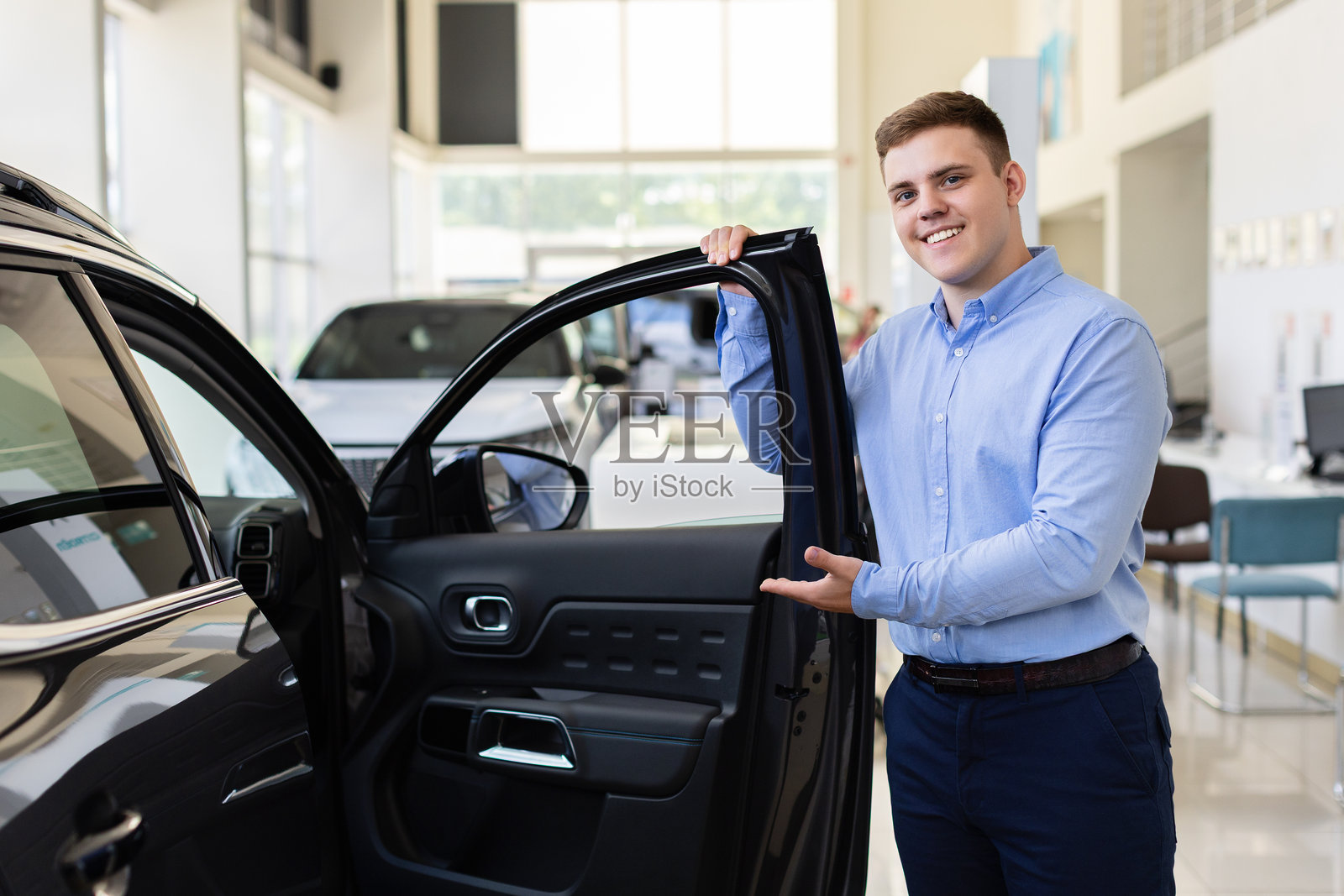 展厅里，一位面带微笑的汽车销售人员正在展示一辆车，车门敞开着。照片摄影图片