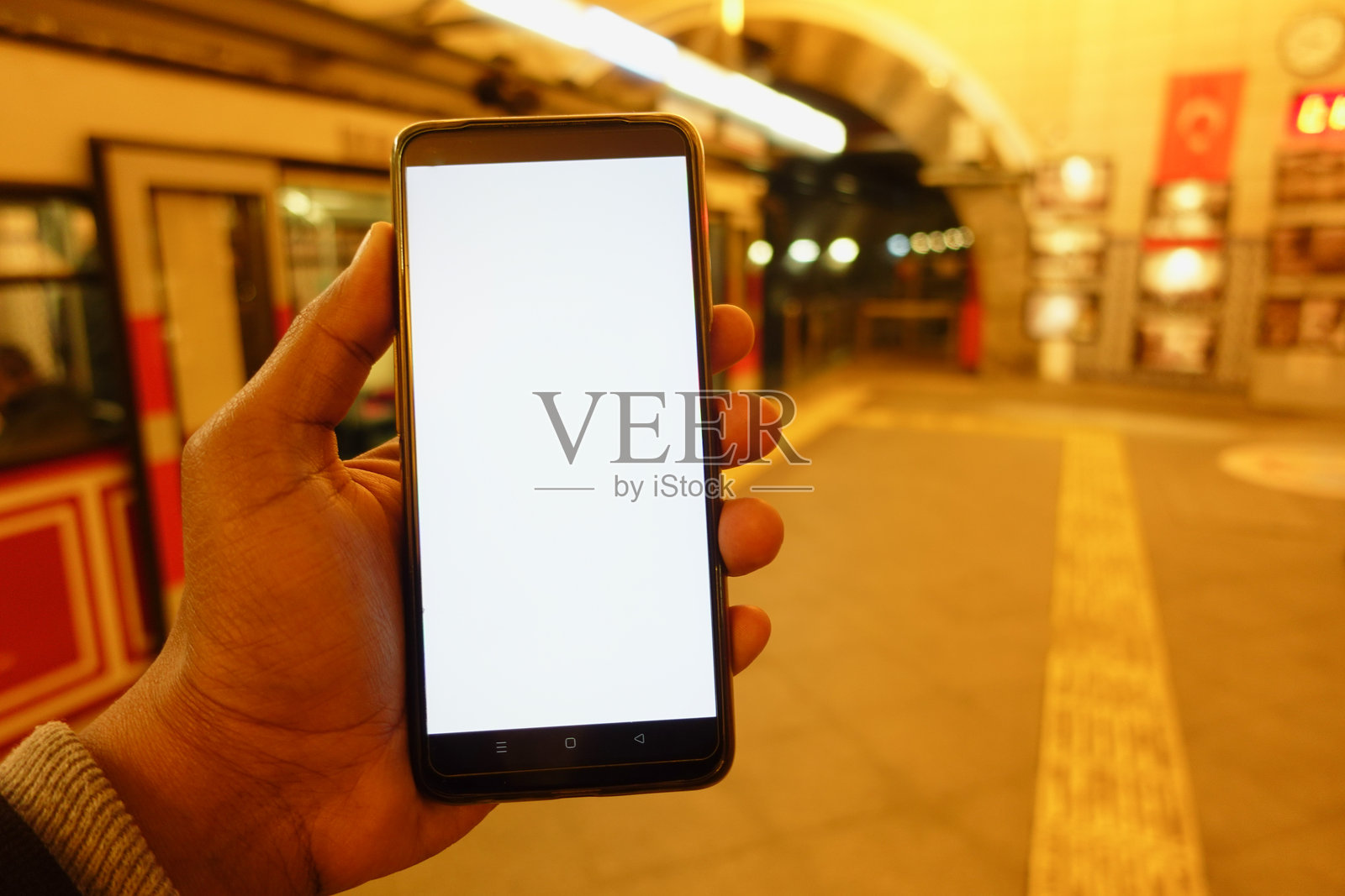 夜间地铁站内，一只手正握着智能手机照片摄影图片