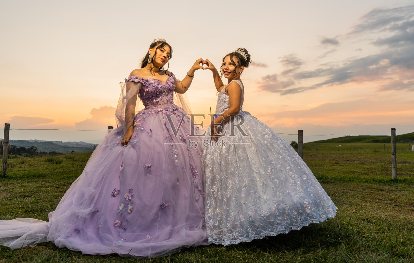 傍晚时分，两位穿着公主裙的女孩在乡间用手比心。照片摄影图片