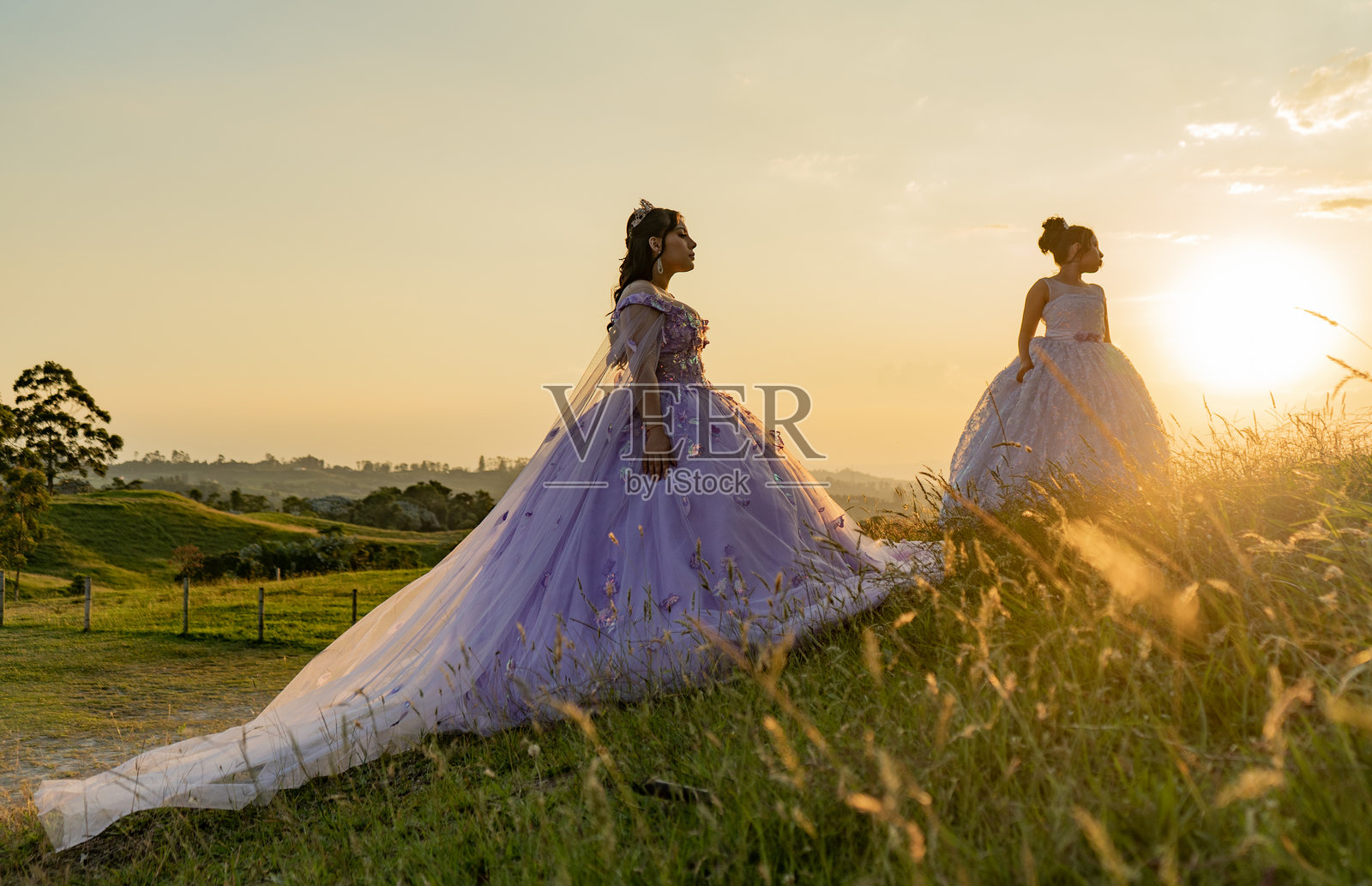 两位身着晚礼服的年轻女子在日落时分的田野里照片摄影图片