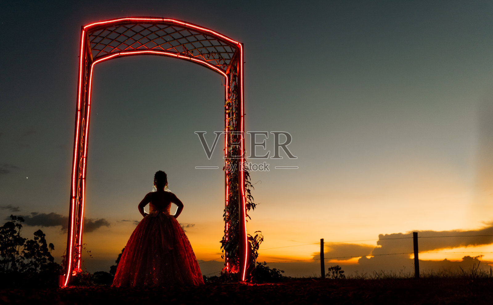 日落时分，身着优雅连衣裙的女孩剪影，在拱门下被照亮。照片摄影图片