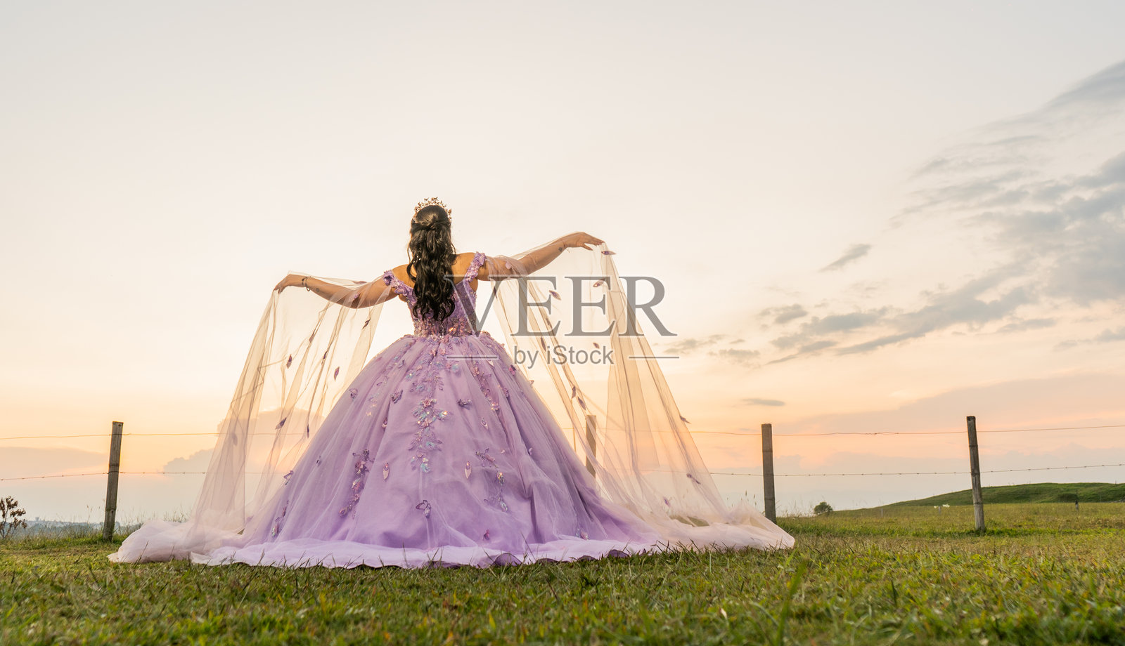 年轻女子身穿丁香色公主裙，在乡村的日落时分展开她的面纱照片摄影图片