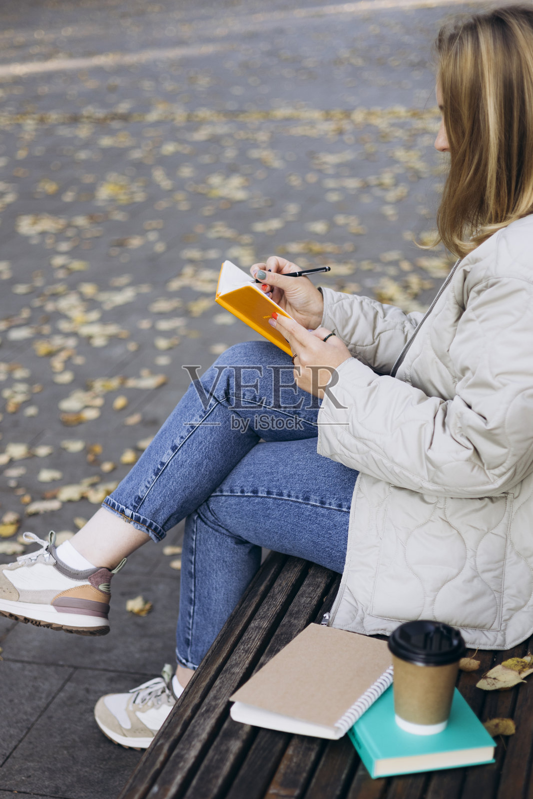 年轻女子秋季公园长椅上写日记。照片摄影图片