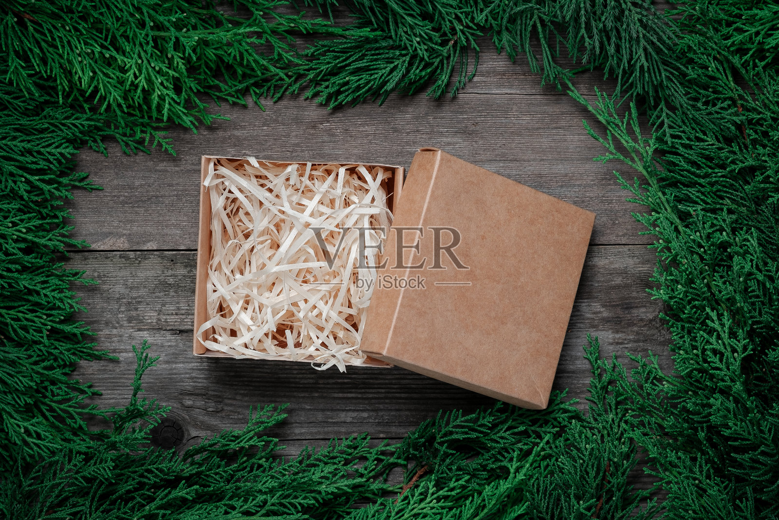 打开的纸板礼品盒，内有木丝填充物，周围环绕着新鲜的绿色雪松枝条。照片摄影图片