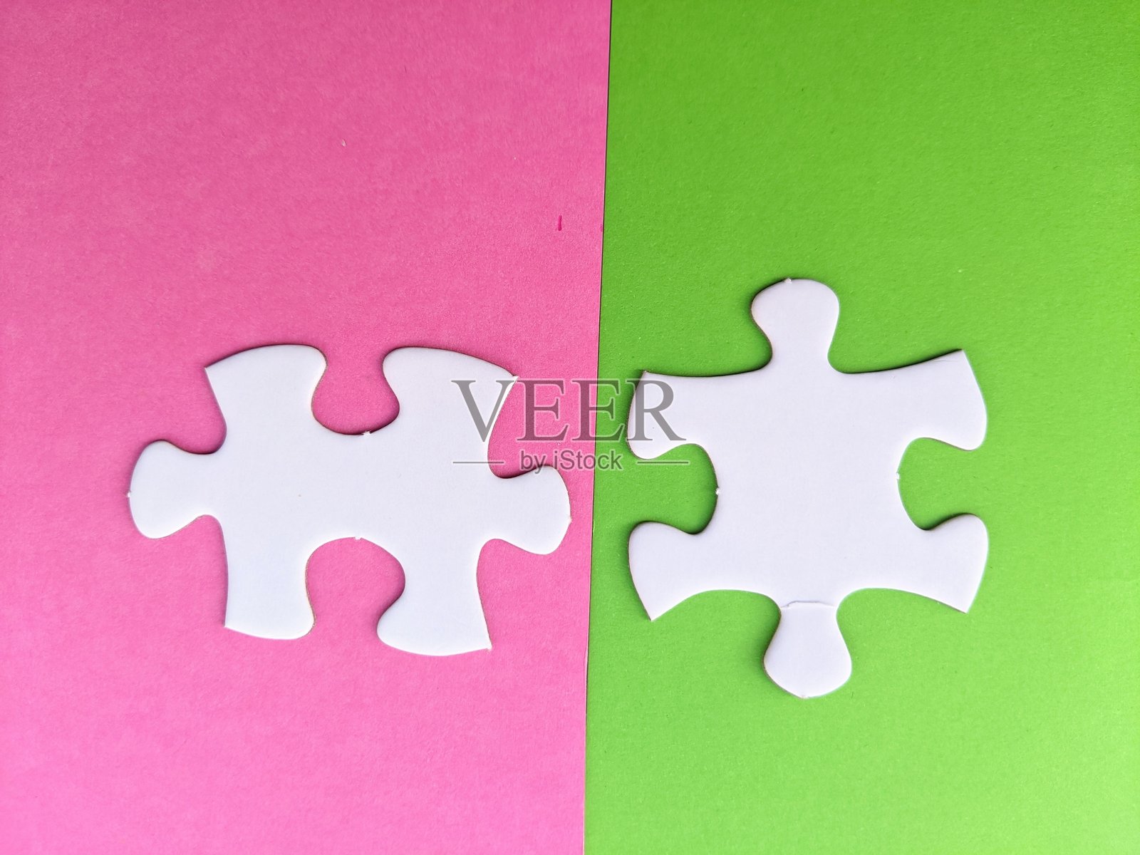 粉色和绿色背景上两个未连接的拼图块。解决问题、团队合作以及整合不同元素以实现和谐整体照片摄影图片