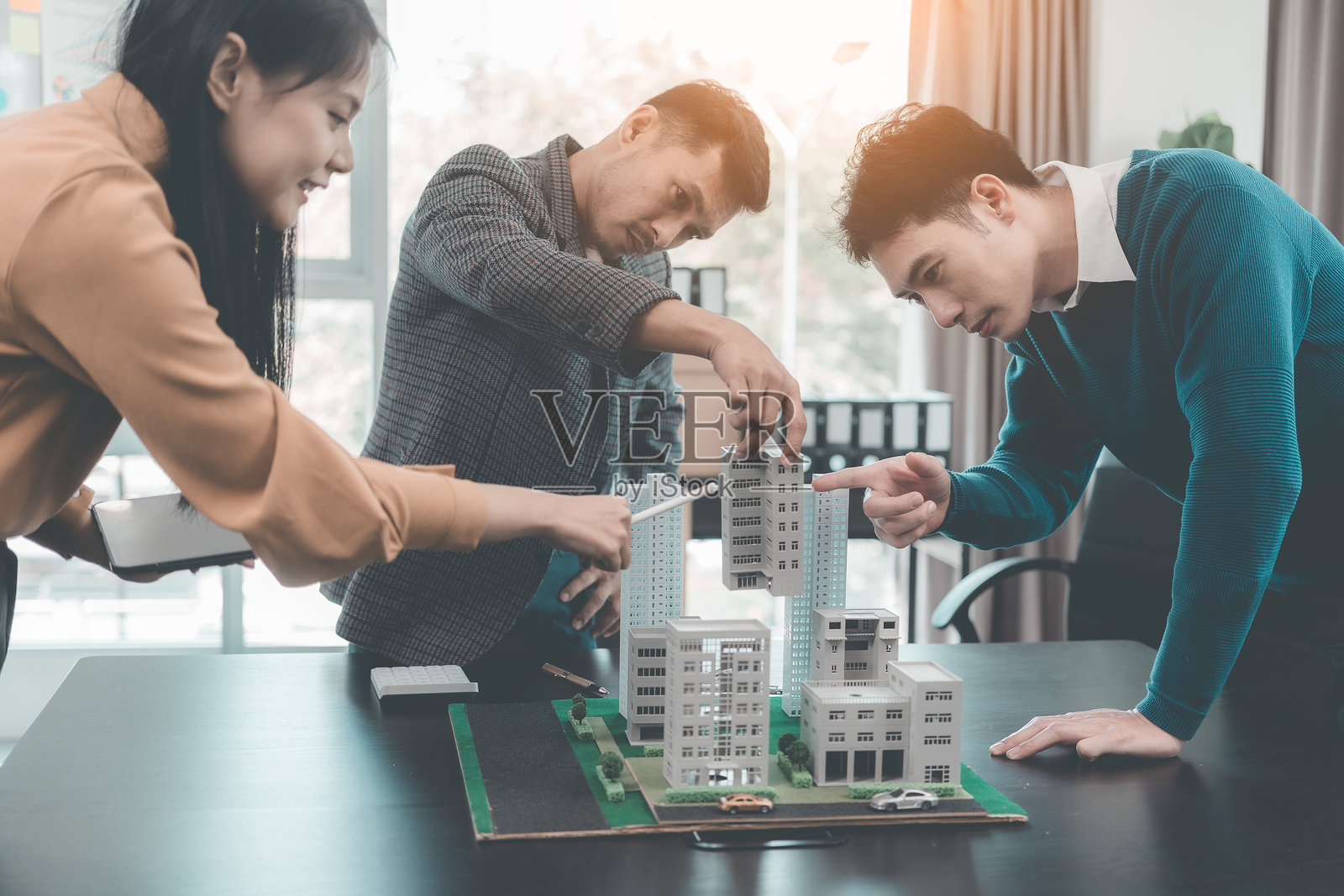 一群年轻的亚洲商界人士在一个办公室里会面，讨论一个住宅房地产项目。一群衣着优雅、专业的个人正在评估一个小型房屋模型。照片摄影图片