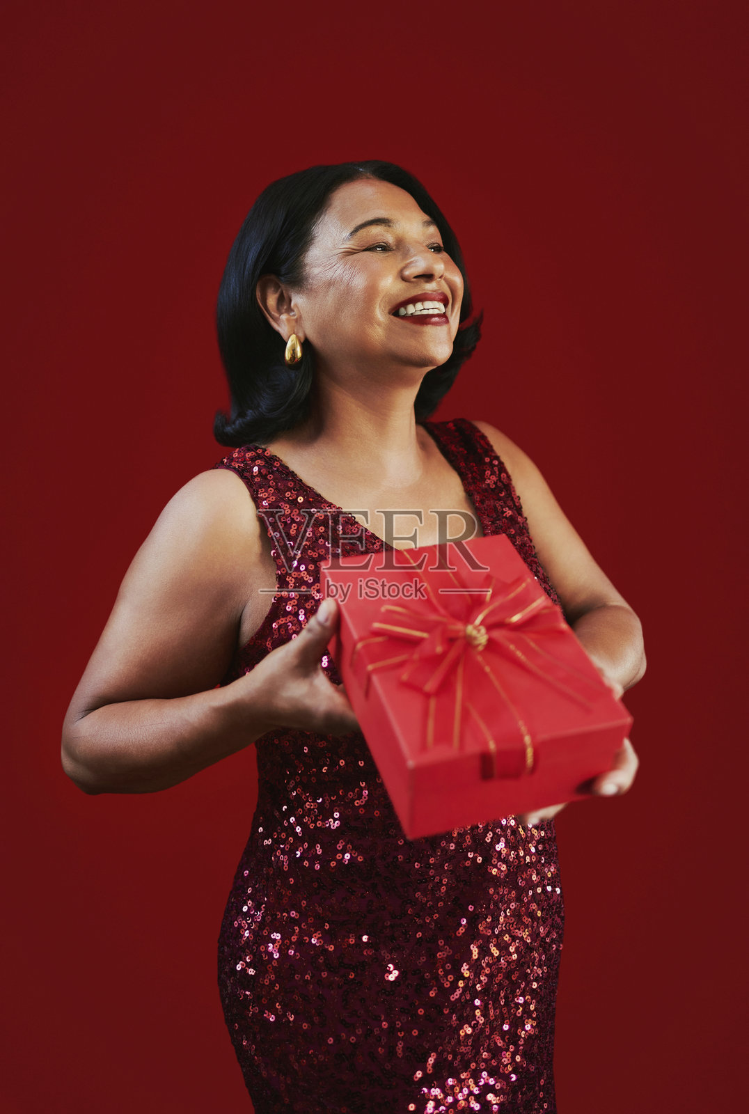 身穿红色亮片连衣裙、手持包装礼物的喜庆女性照片摄影图片