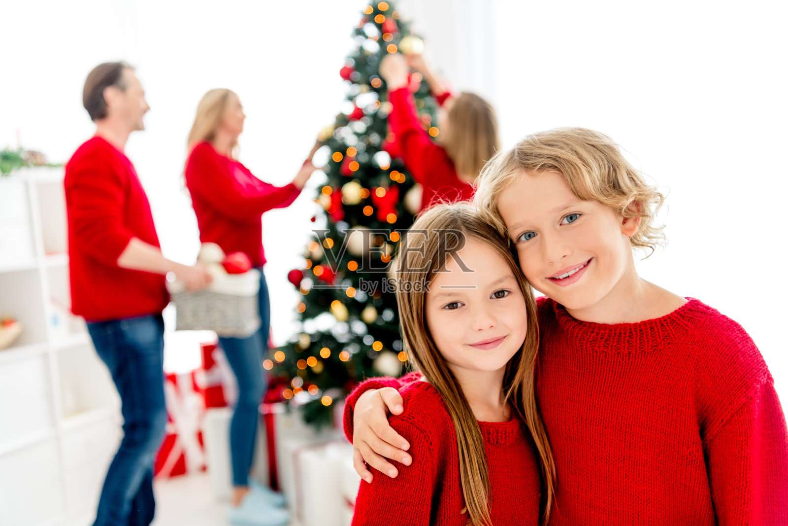 快乐的一家人在家中温馨地享受圣诞早晨，孩子们和父母正装饰着圣诞树，挂上饰品和彩灯。照片摄影图片