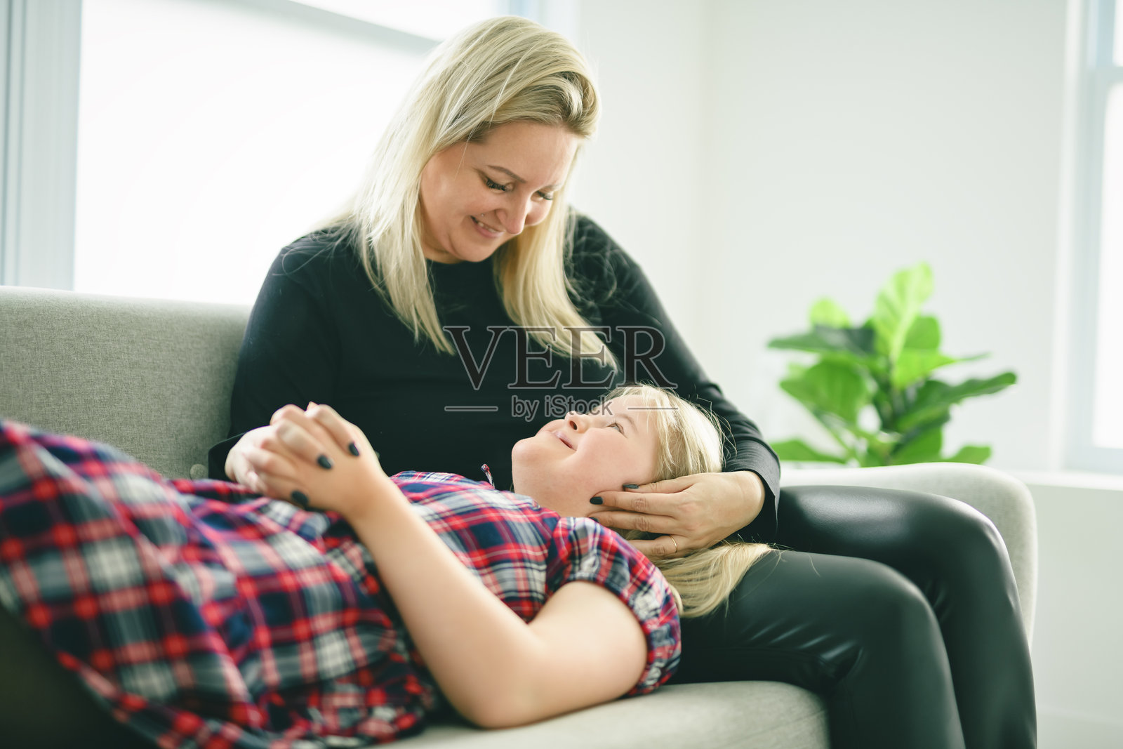 母亲和患有唐氏综合征的可爱女儿在家里的沙发上照片摄影图片