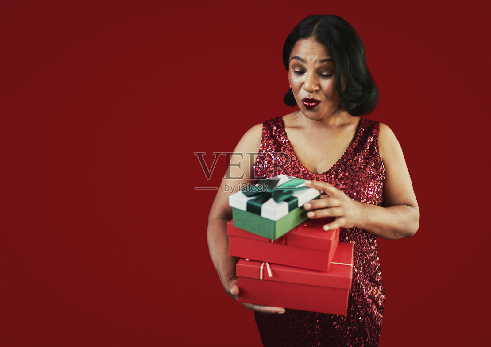 年轻女子手持包装好的圣诞礼物，背景为红色，充满节日喜庆气氛照片摄影图片