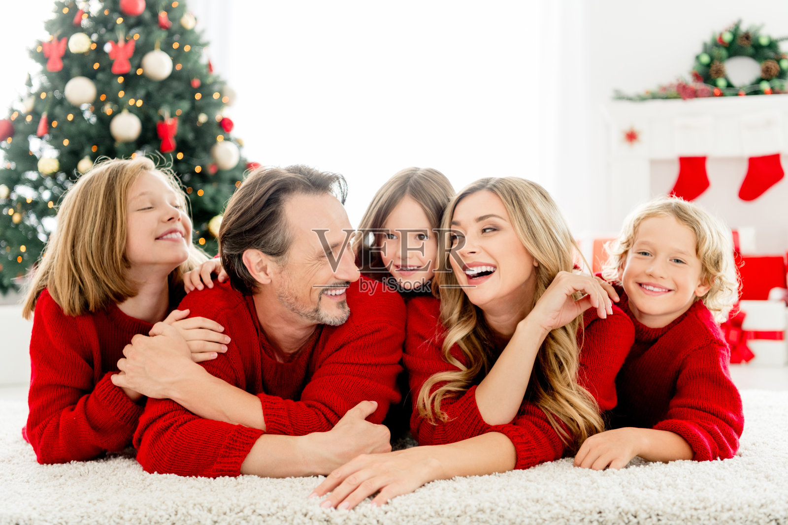 家人在家庆祝圣诞节，父母和孩子们穿着红色毛衣，面带笑容，旁边有圣诞树。照片摄影图片