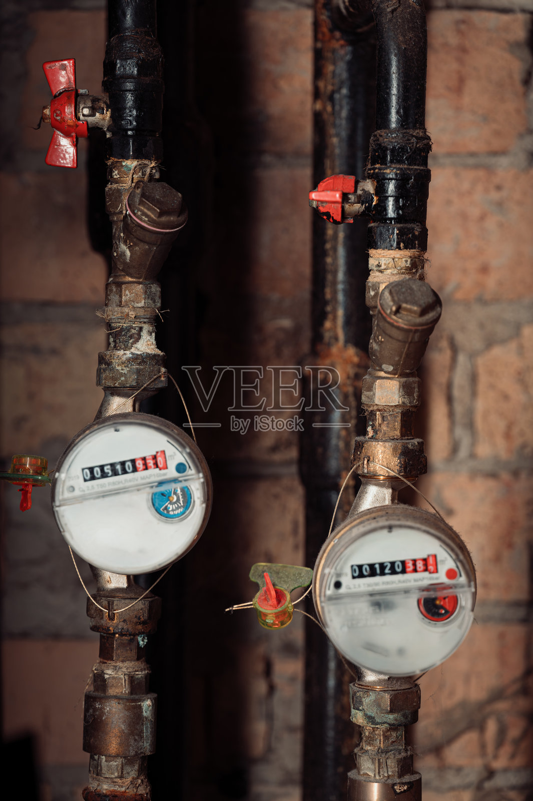 深色管道上的工业水表配有红色阀门，背景是石墙照片摄影图片