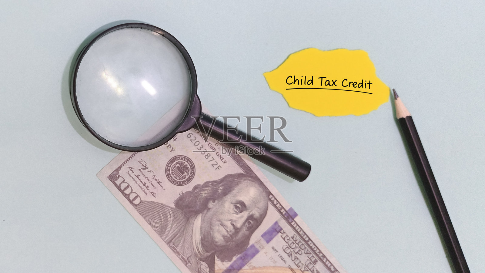用放大镜检查旁边的百元钞票上的儿童税收抵免。照片摄影图片