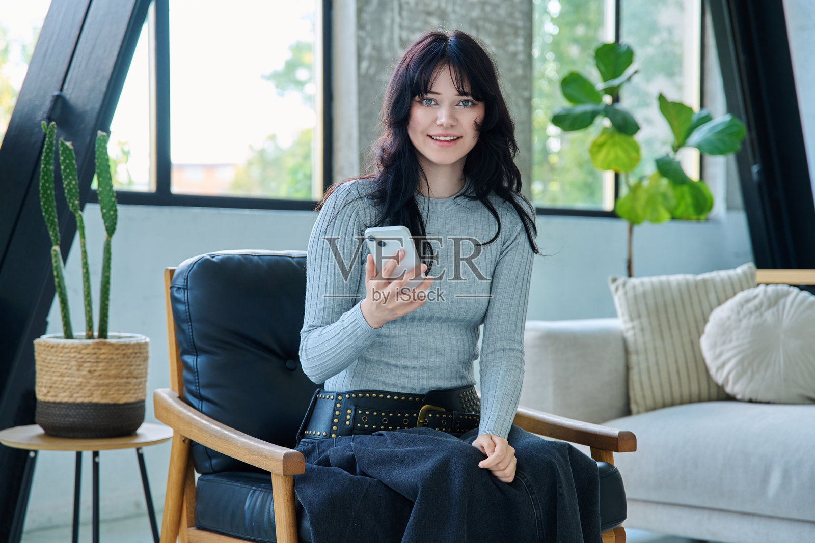 年轻女子坐在椅子上，手持智能手机，看向镜头，居家室内肖像照片摄影图片