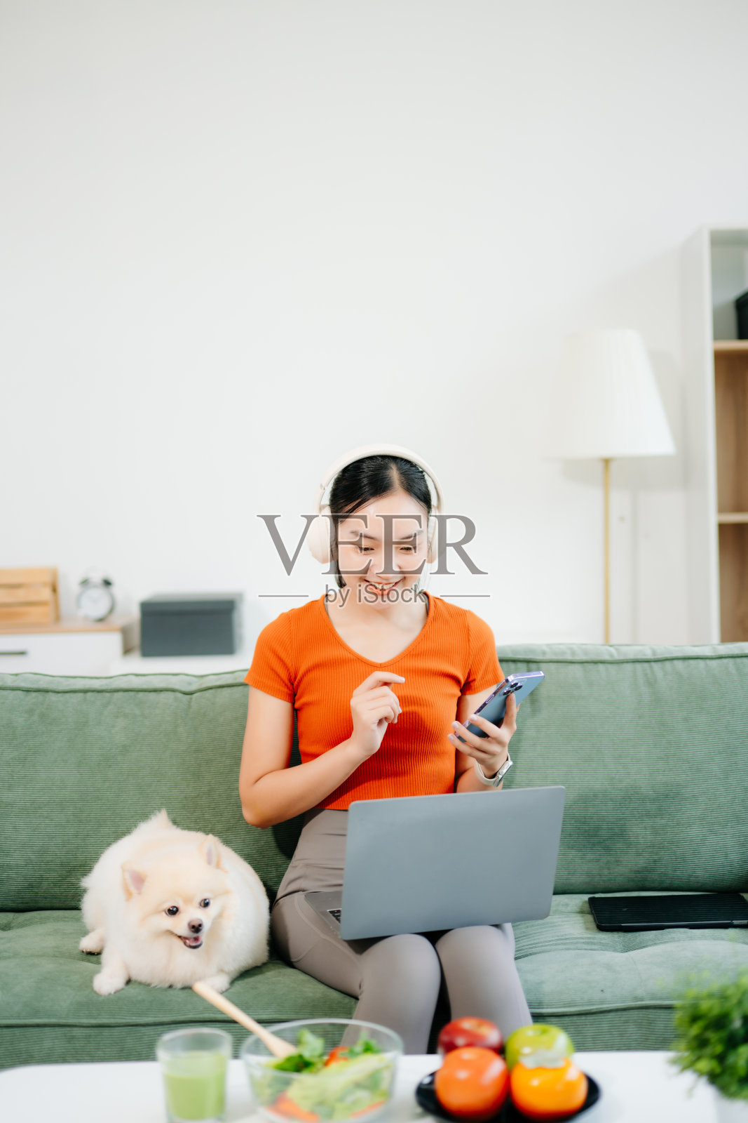 明亮现代客厅里，年轻女子坐在白色沙发上，怀里抱着一只白色小狗，脸上洋溢着喜悦，正在室内工作。照片摄影图片