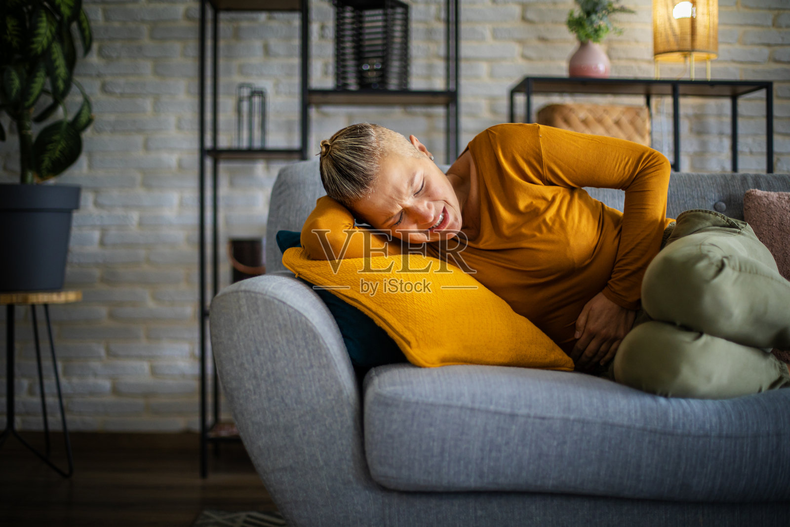 女子躺在沙发上，腹部疼痛照片摄影图片