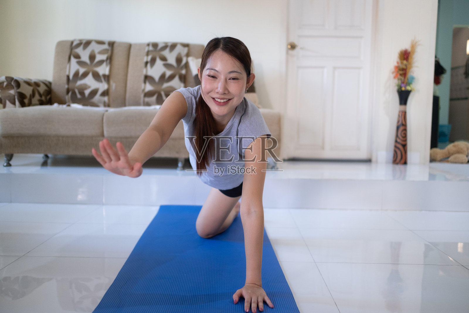 一位女士正在客厅的蓝色瑜伽垫上做瑜伽照片摄影图片