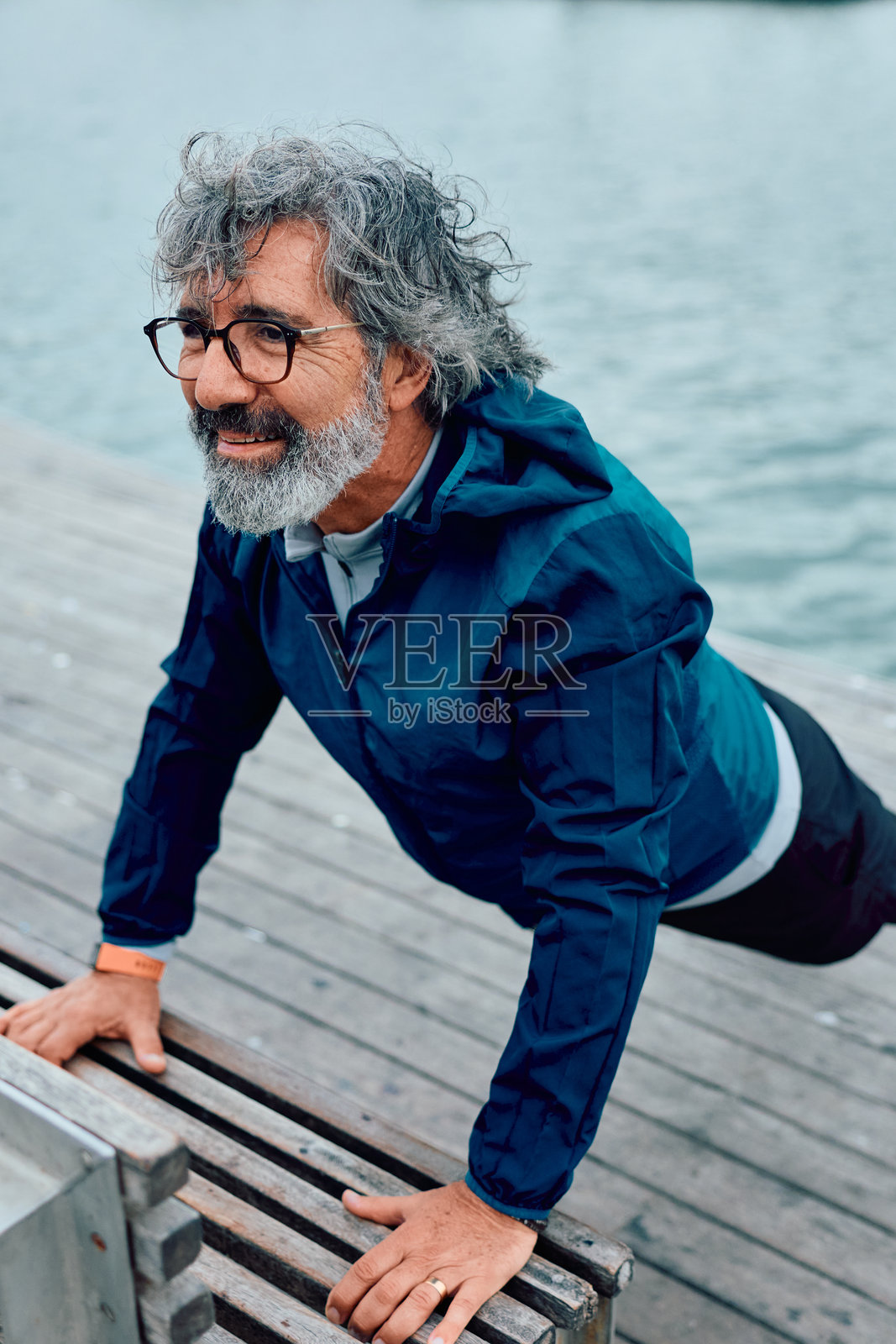 一位老年男子在水边的木板路上做俯卧撑照片摄影图片