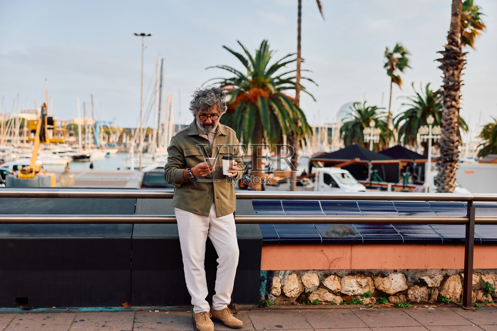 一位成熟的成年男子在港口一边喝咖啡一边查看智能手机照片摄影图片