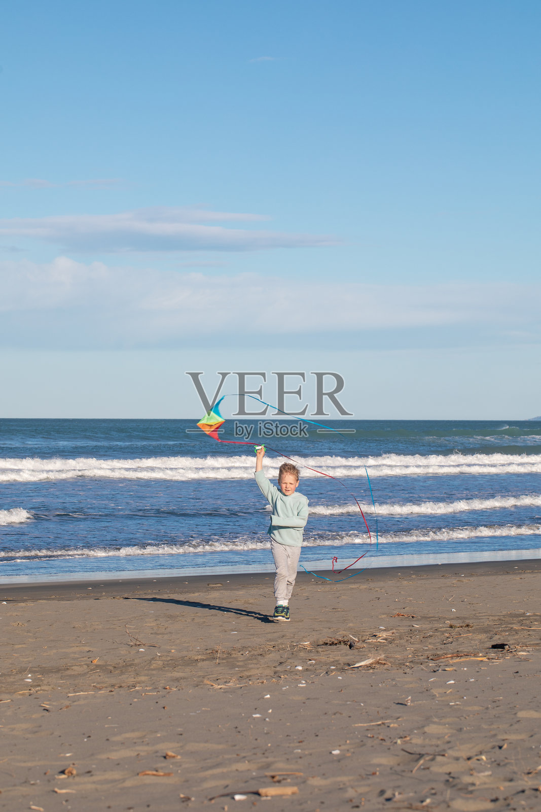 快乐的小男孩在海滩上奔跑放飞色彩鲜艳的风筝。适合儿童的户外趣味活动照片摄影图片