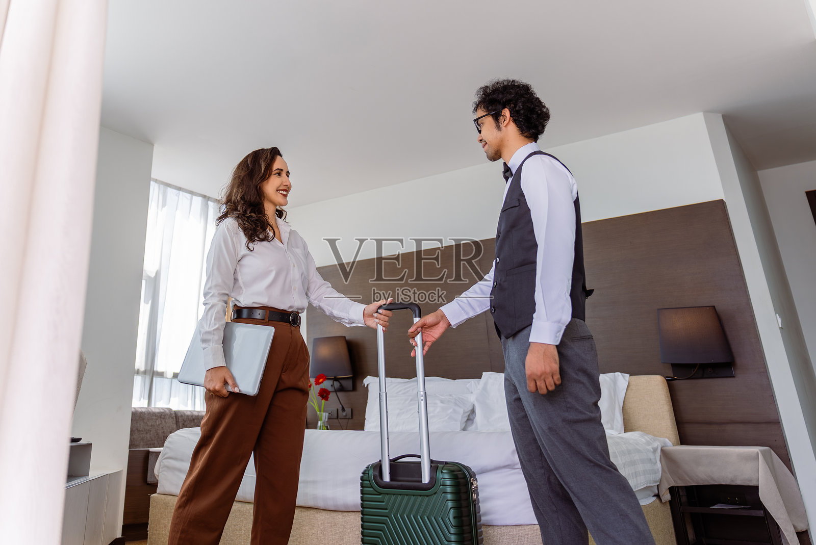 一位面带微笑的酒店员工在现代豪华套房的大窗户旁，协助商务旅客拿行李，迎接旅客的到来。照片摄影图片