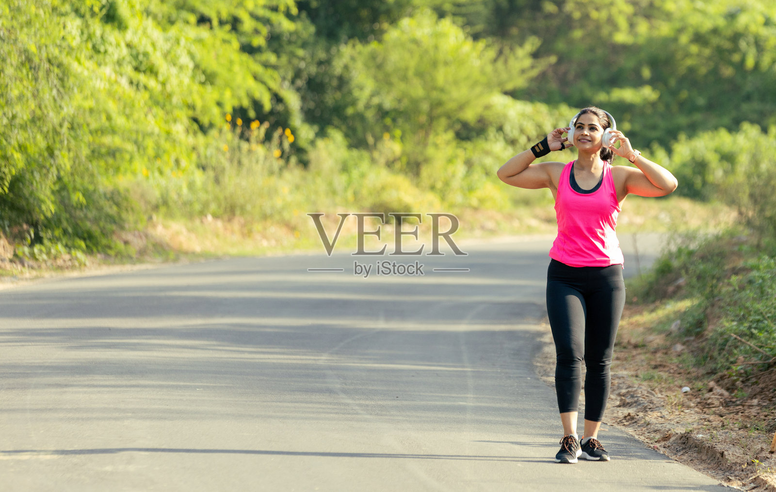 快乐的印度女性佩戴无线耳机和智能手表在户外跑步照片摄影图片