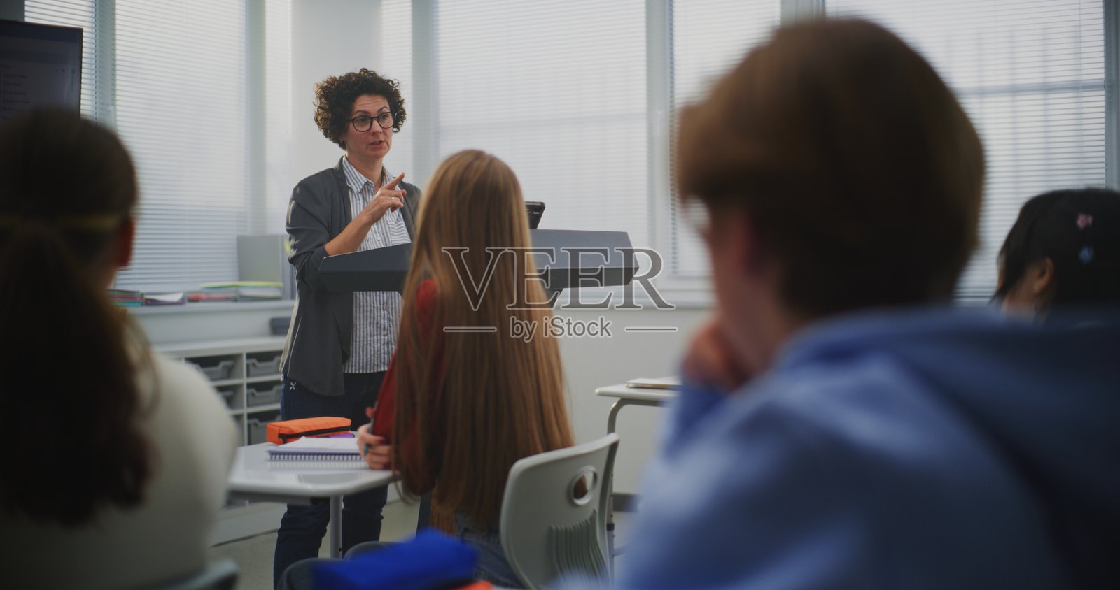 自信的女教师指导专心致志的学生们编程，并指向屏幕上的代码行照片摄影图片