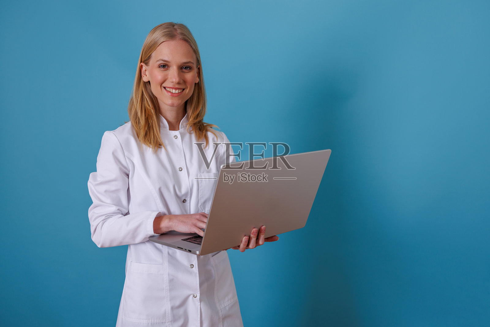 一位年轻的女医生穿着白色实验服，站着在笔记本电脑上打字，脸上带着微笑照片摄影图片