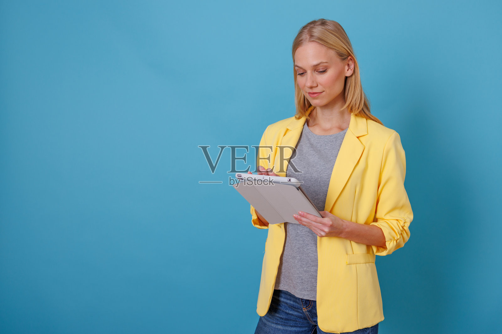 年轻女性使用数字平板电脑进行专业工作，在空白蓝色背景上查看内容照片摄影图片