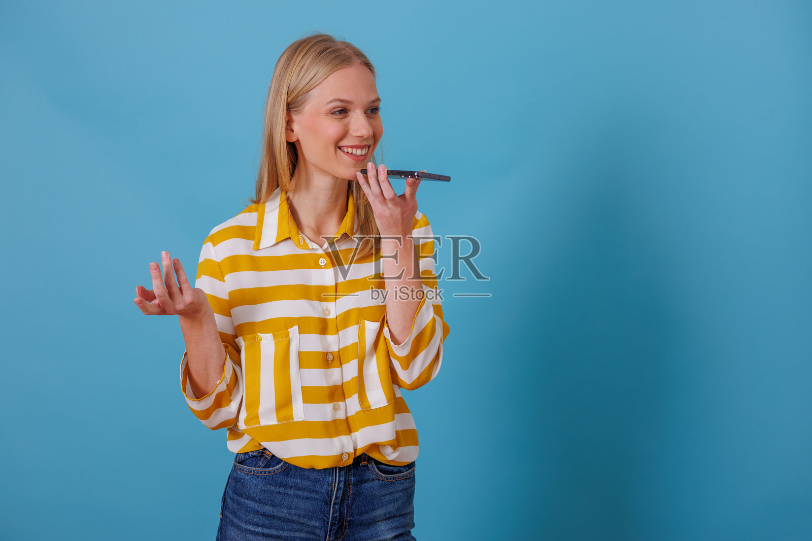 年轻女性在蓝色背景下使用智能手机录制语音消息进行沟通照片摄影图片