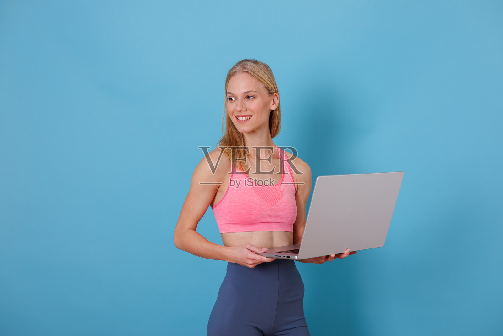 穿着运动服的女子在家中手持笔记本电脑，面带微笑，准备进行在线健身训练照片摄影图片