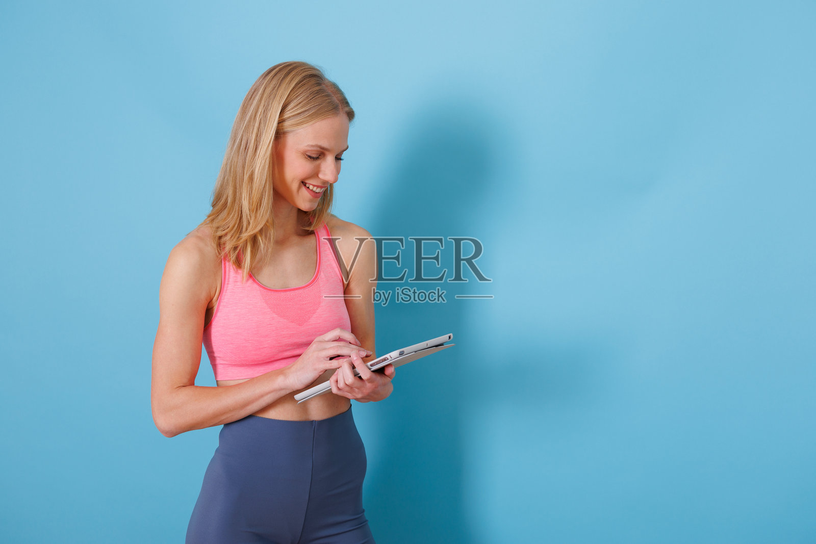 身穿运动服的女性在蓝色背景下使用平板电脑进行健身追踪和在线锻炼照片摄影图片
