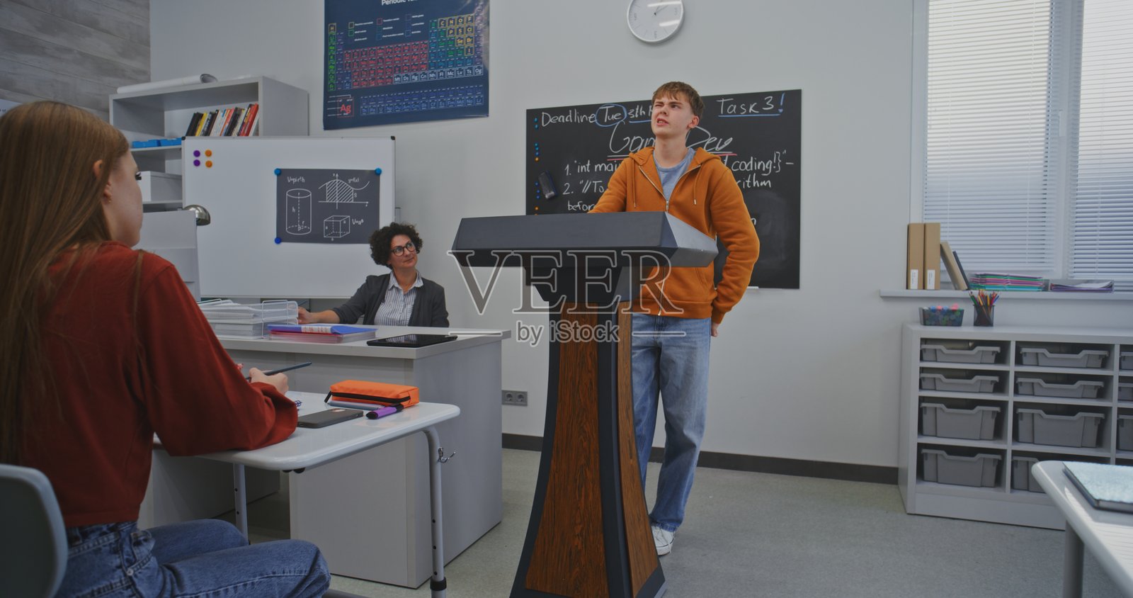 穿着橙色帽衫的学生自信地站在讲台后，面对着同学们发表演讲照片摄影图片