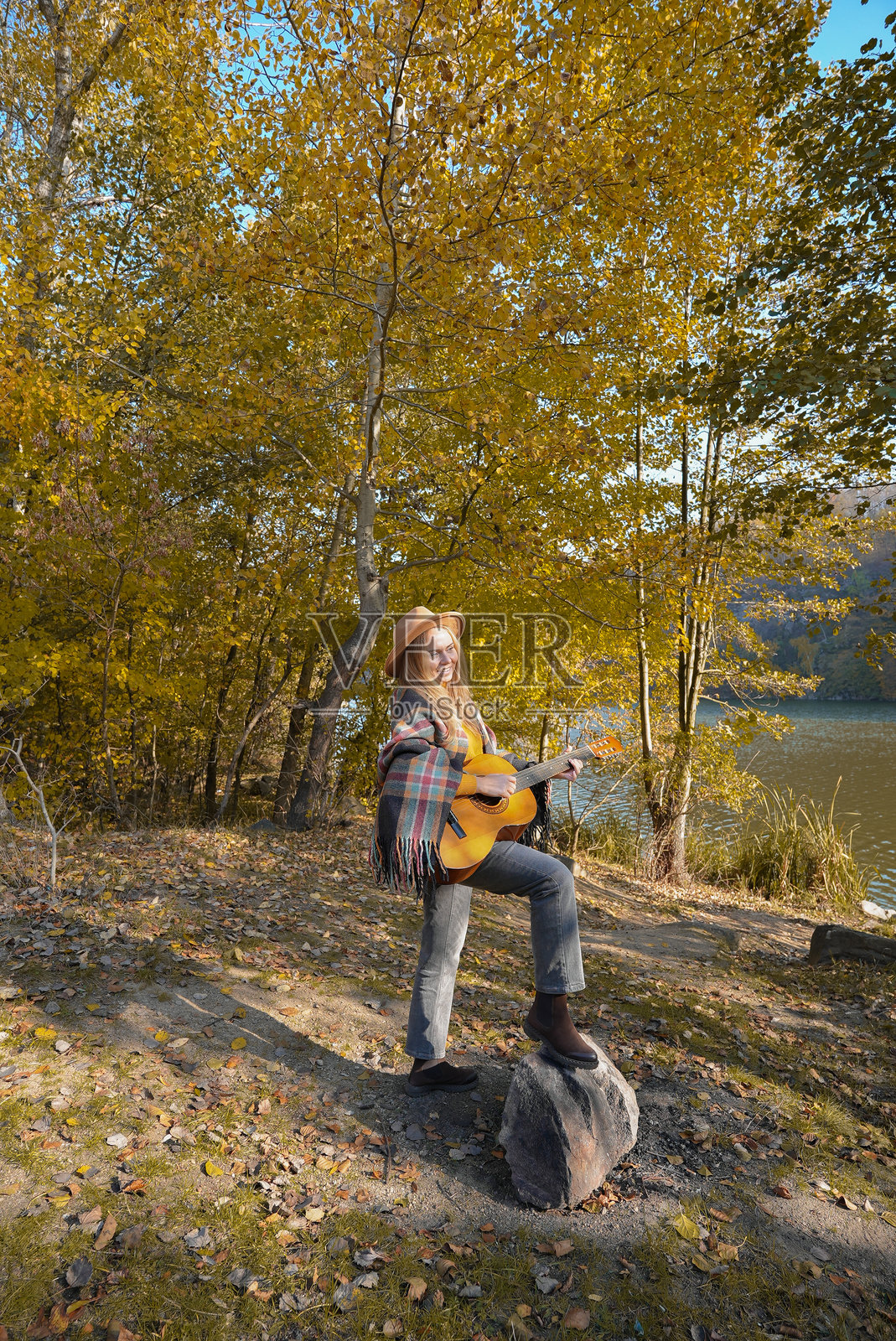 微笑的白人艺术家在秋季公园里弹奏木制原声吉他肖像。年轻的词曲作者在秋季的自然户外演奏弦乐器，爱好音乐疗愈。照片摄影图片