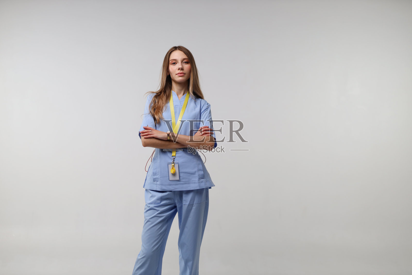 一位自信的年轻白种女护士，身穿蓝色护士服，佩戴身份识别证，背景为白色。照片摄影图片