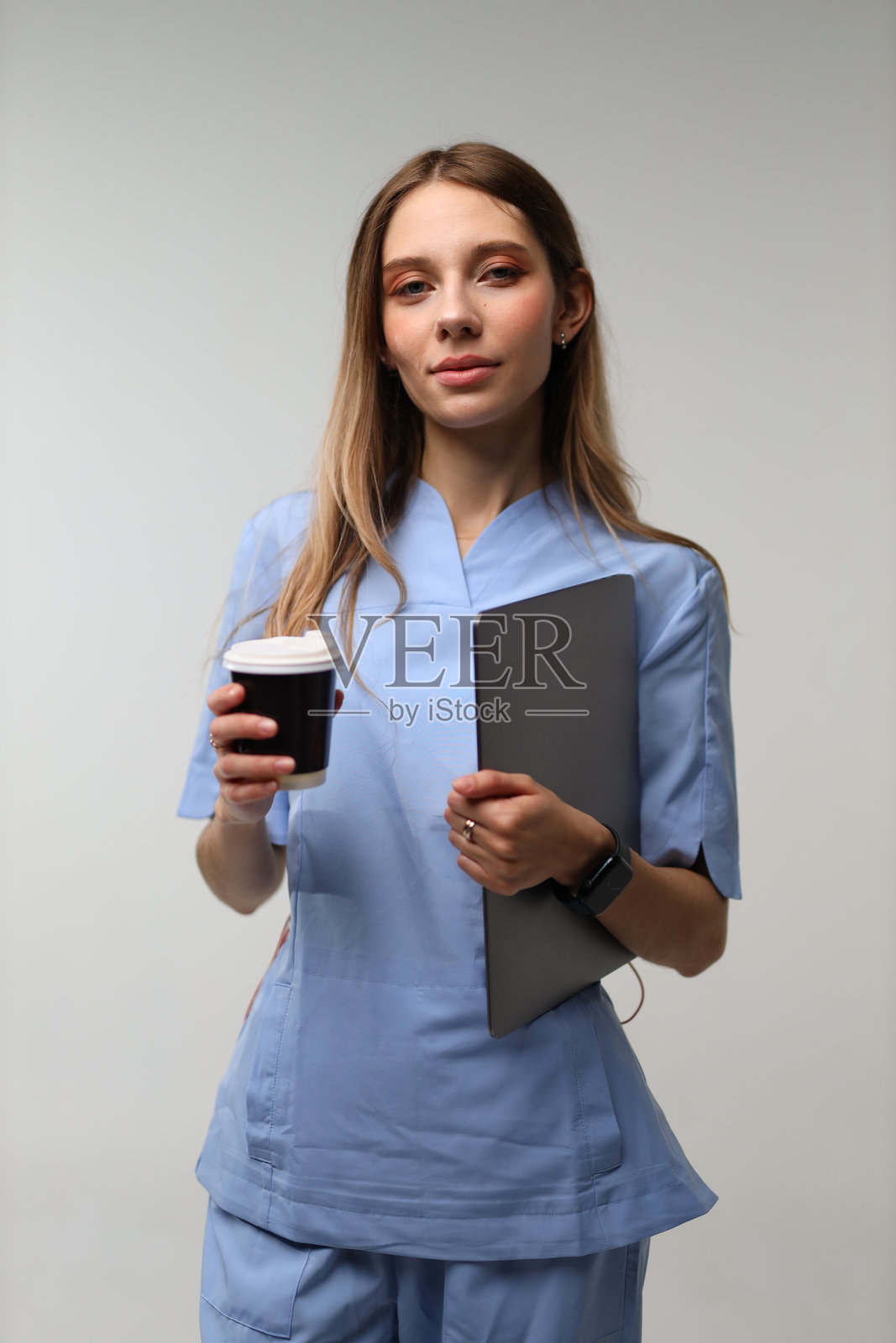 穿着蓝色工作服的年轻白人女护士，手持咖啡和文件夹照片摄影图片