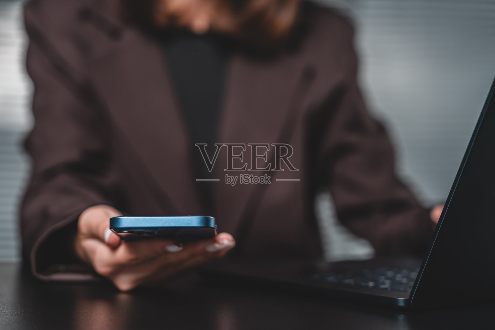 女商人使用智能手机和笔记本电脑在工作场所进行多任务处理，背景虚化，体现科技与沟通的概念。照片摄影图片