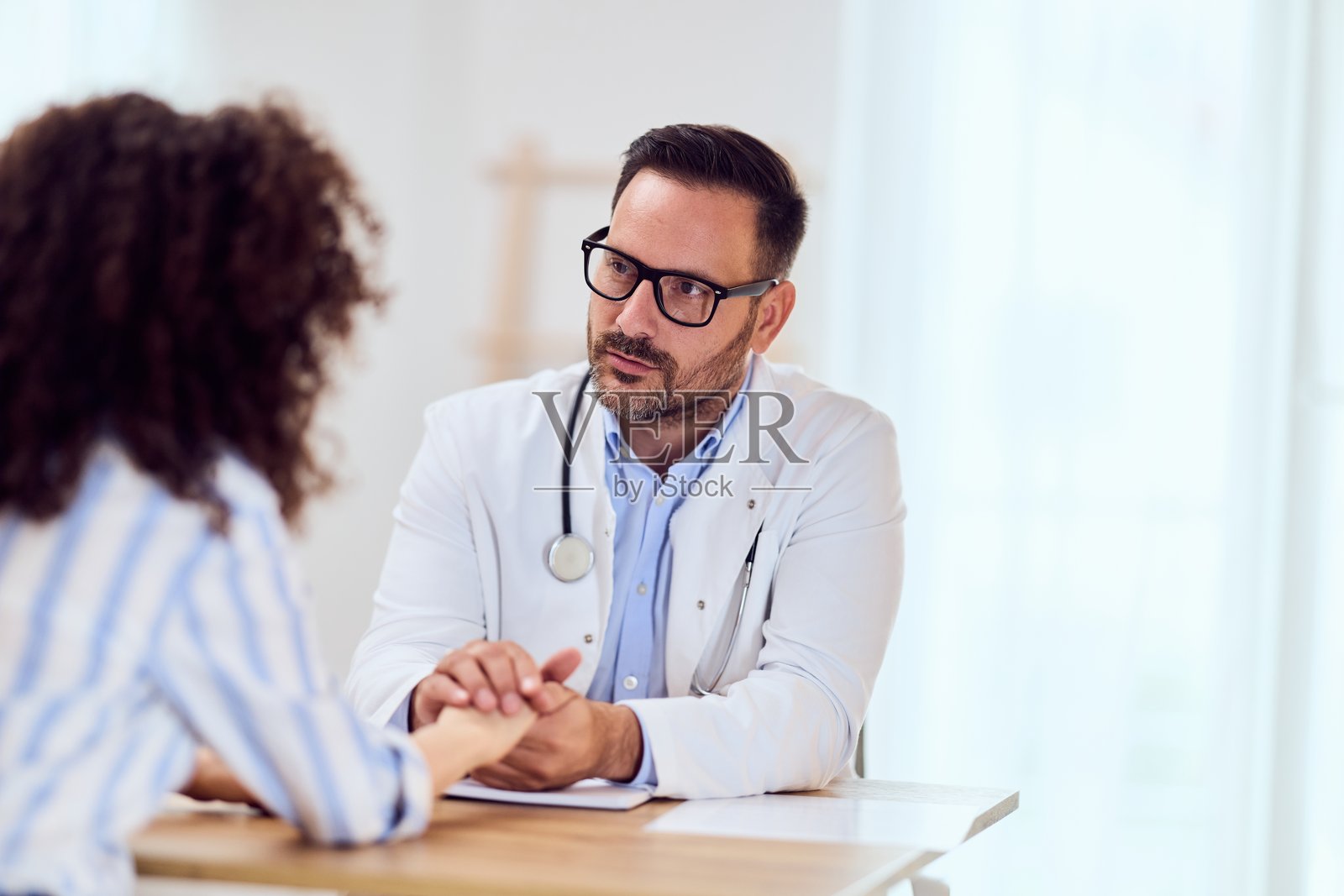 慈祥的医生在明亮的诊所里，用听诊器为就诊的病人看诊照片摄影图片