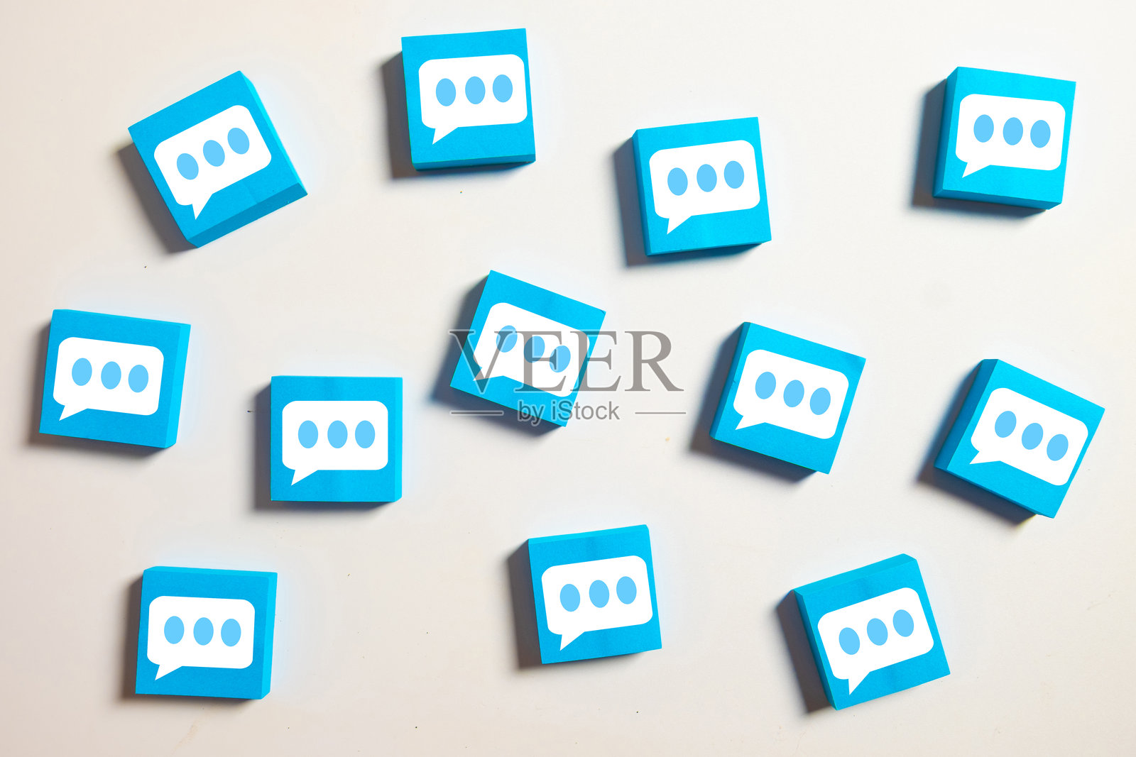 白色背景上散落着多个带有语音气泡图标的蓝色方块，象征着沟通、社交媒体、消息和评论。照片摄影图片