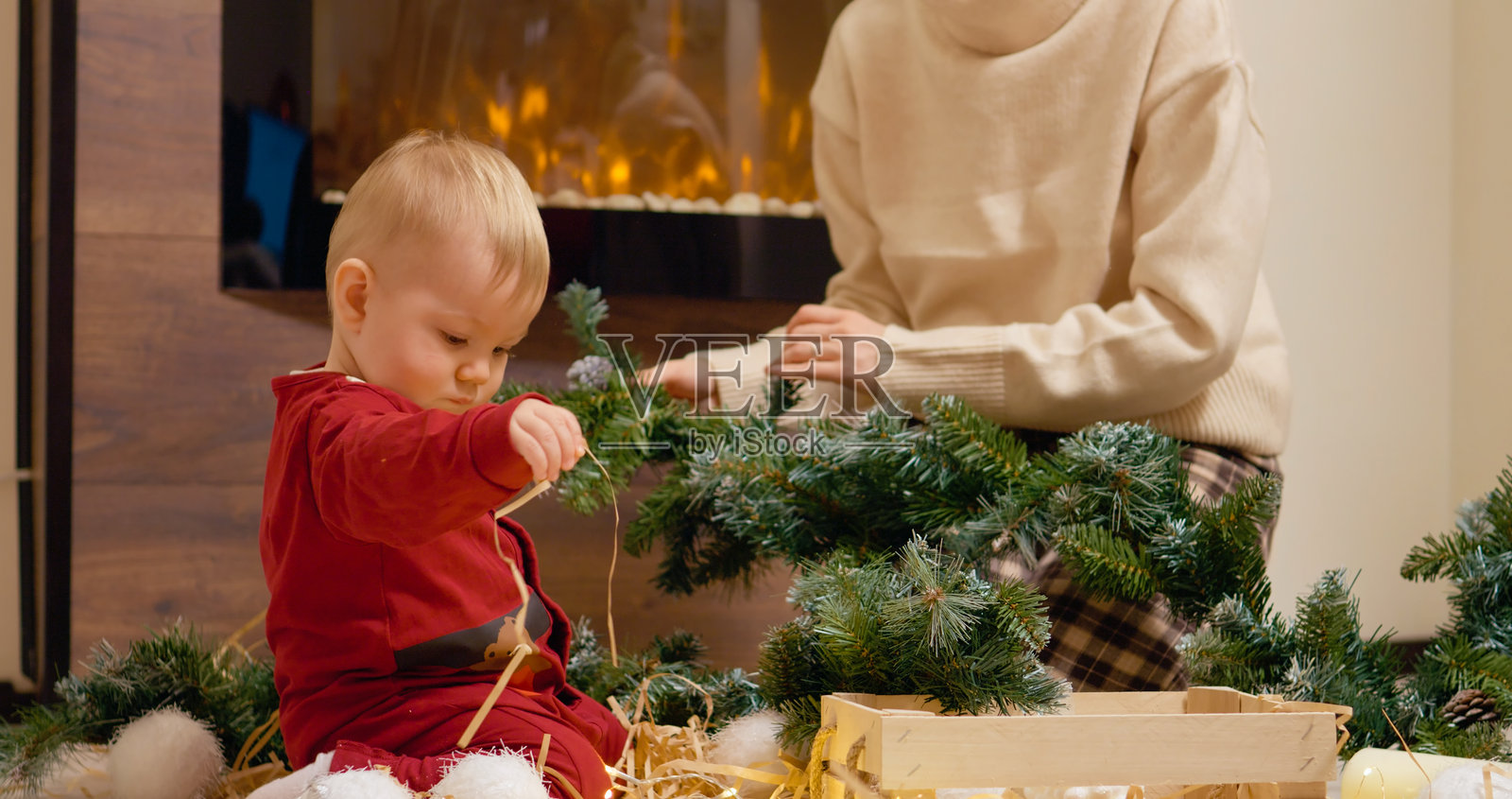 小男孩在妈妈布置圣诞树时，开心地玩着圣诞装饰品照片摄影图片