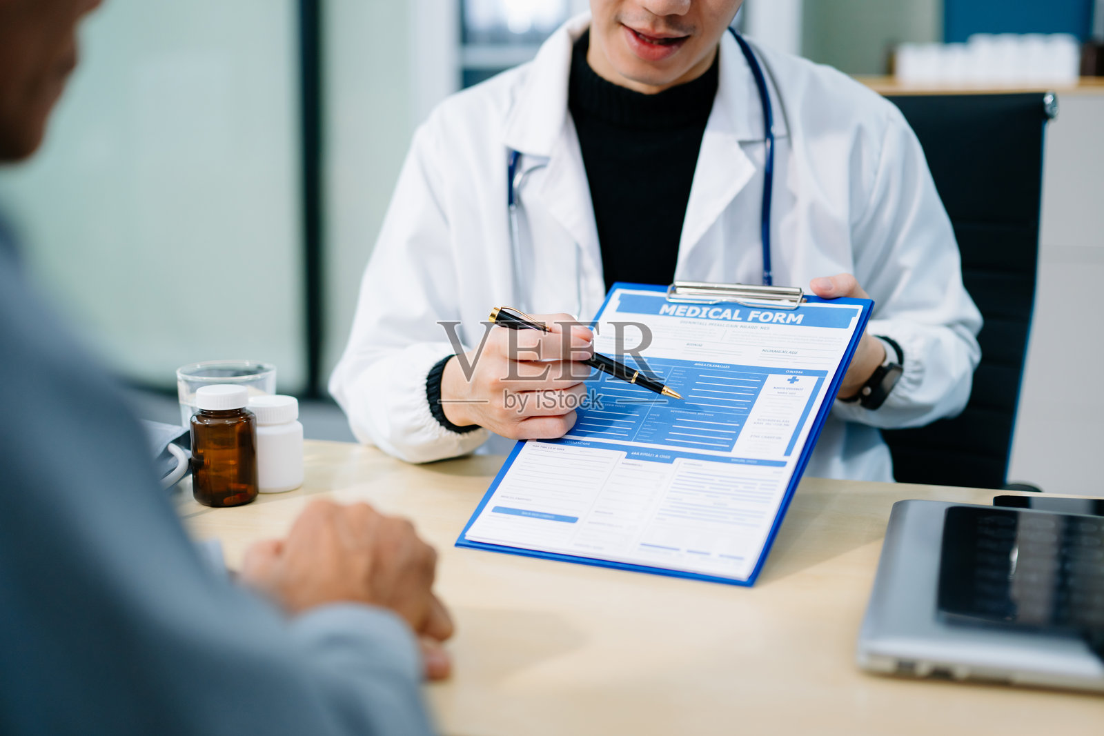 一位亚洲医生在明亮的诊所办公室咨询病人时，指向一份医疗表格。医疗保健、保险的概念照片摄影图片