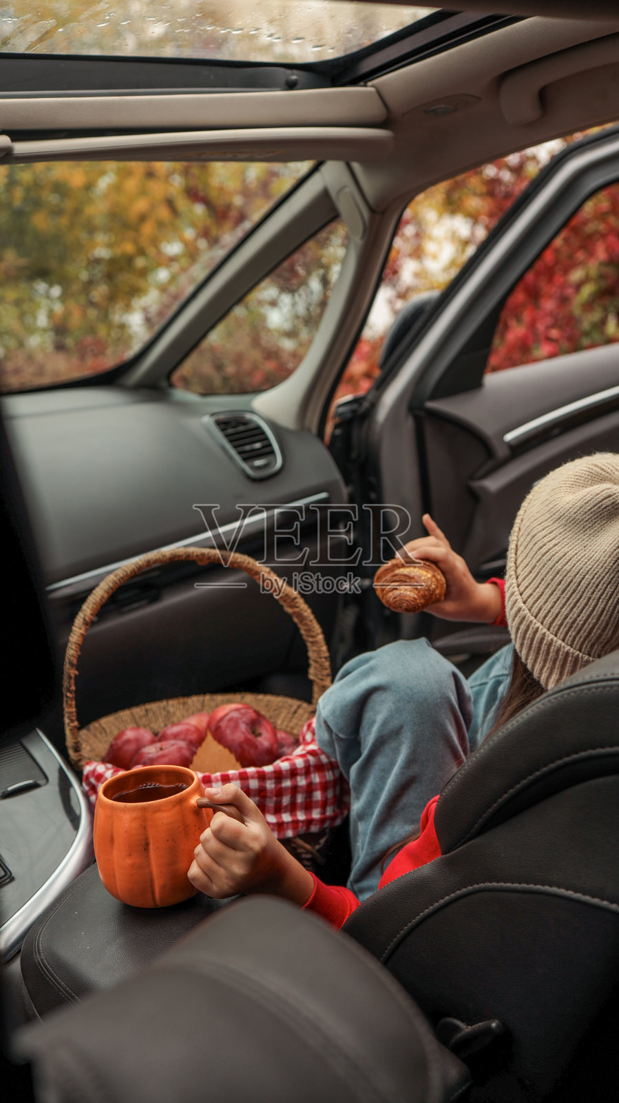 舒适的秋日野餐在车内进行，一个孩子正享用着牛角包和茶。照片摄影图片