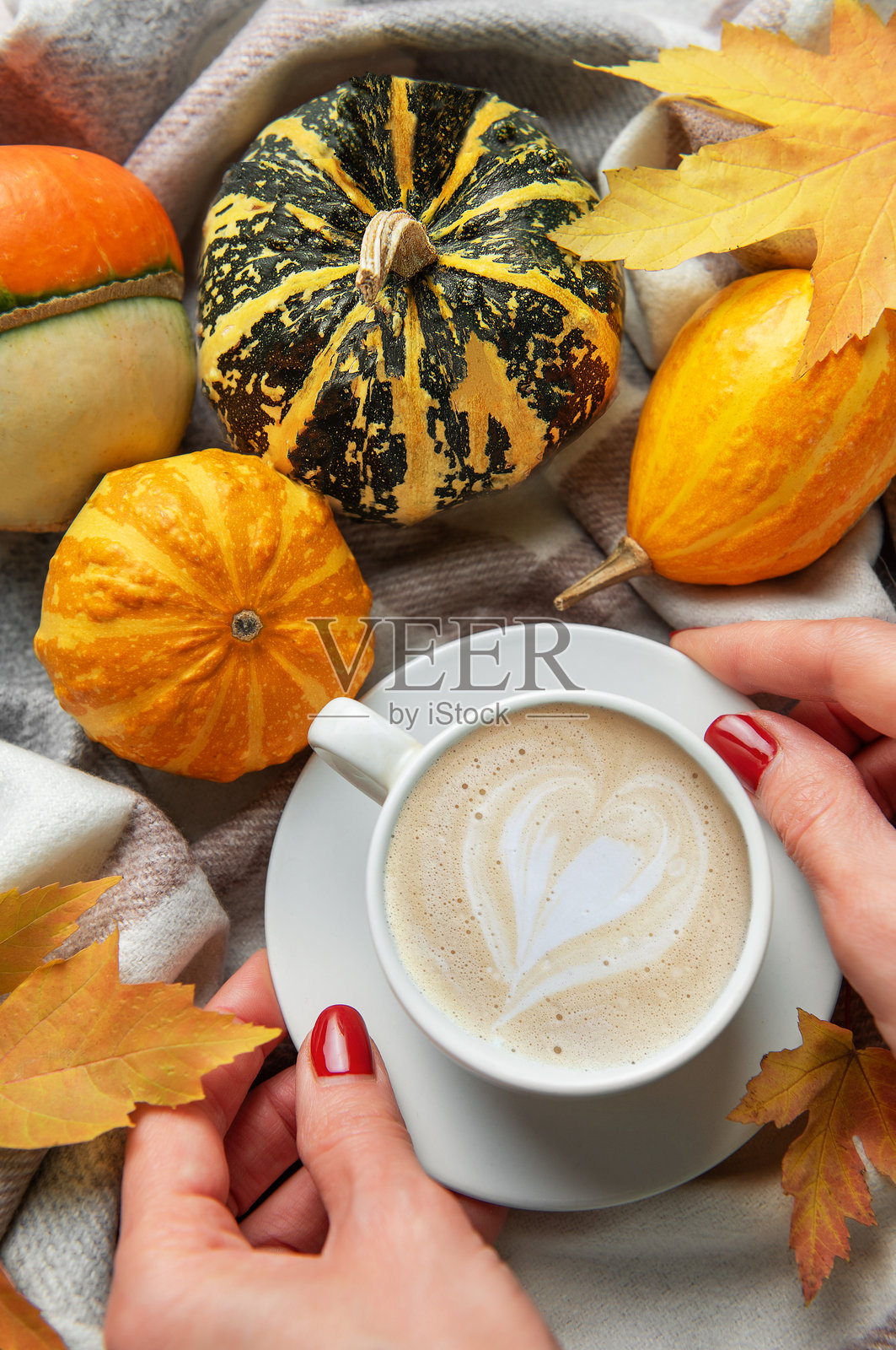 双手捧着咖啡，咖啡上是爱心拉花，周围环绕着秋季南瓜照片摄影图片