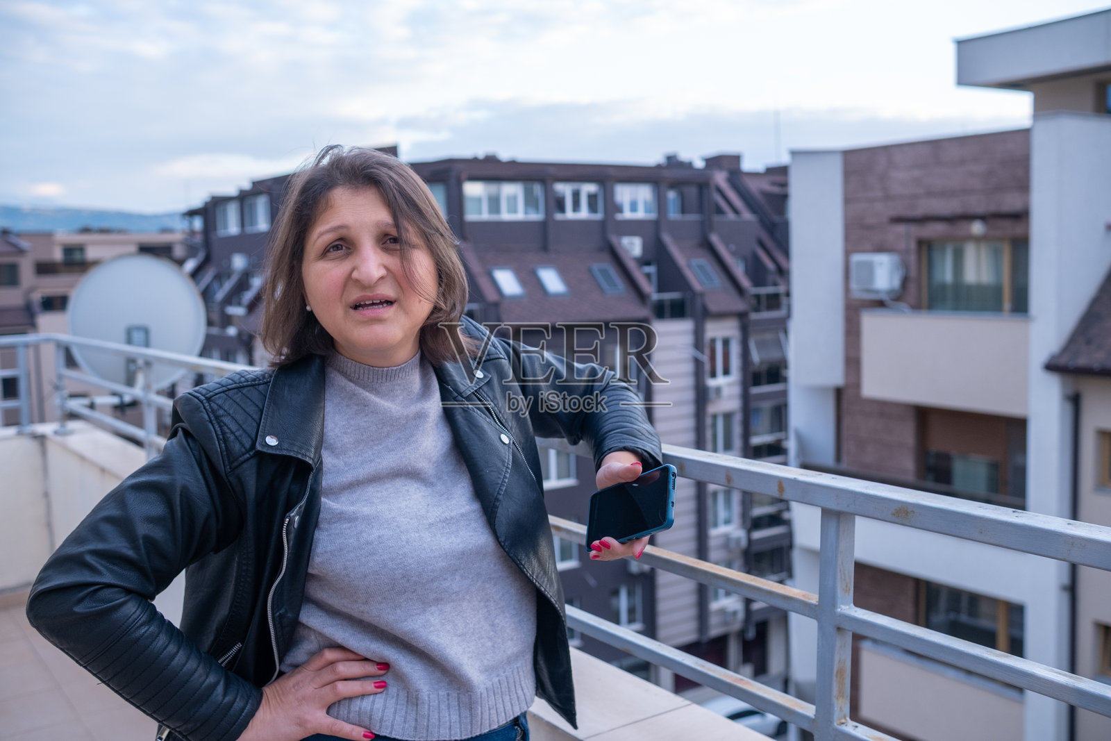 一位紧张的女士愁眉不展地望着镜头，背景是城市屋顶。照片摄影图片