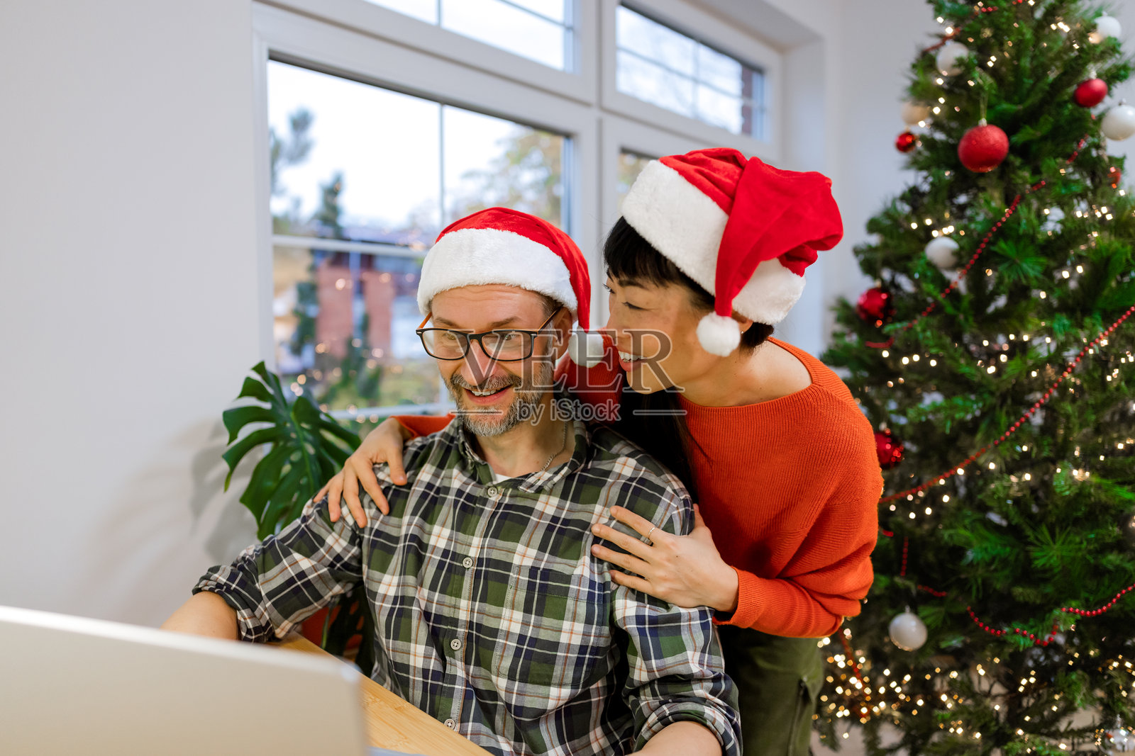 女人拥抱伴侣，伴侣暂停工作，一同欣赏圣诞装饰，温馨时刻照片摄影图片