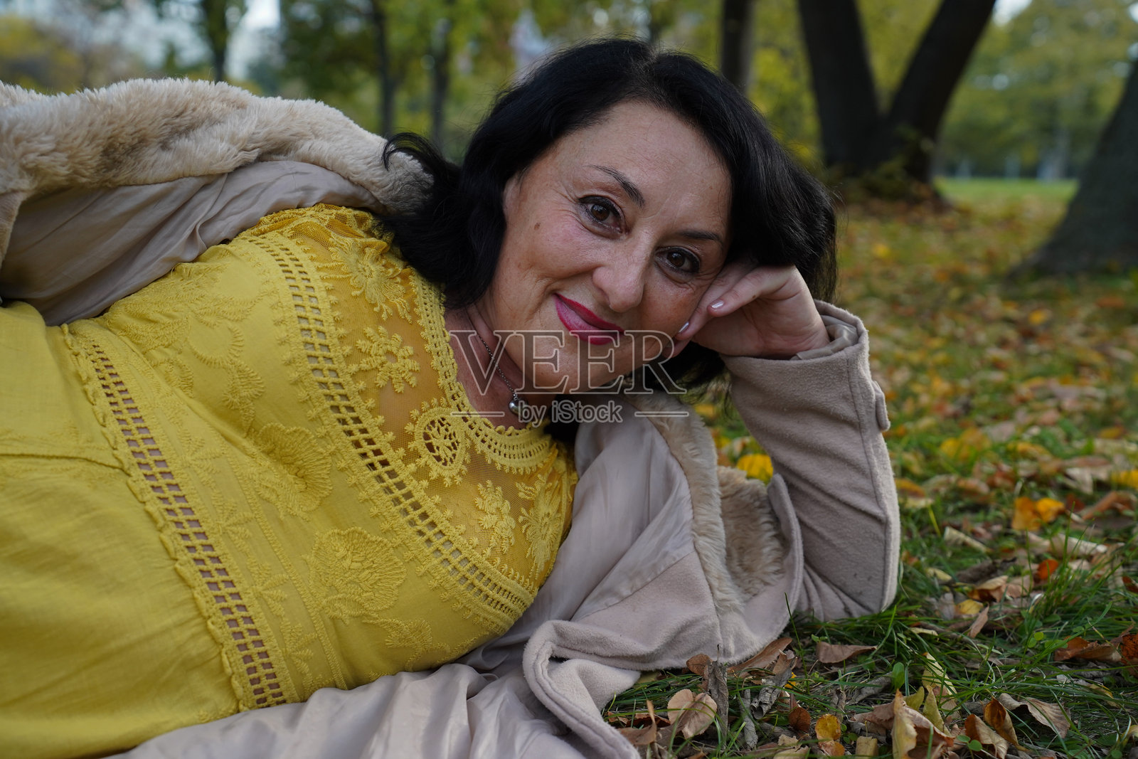 身穿黄裙的女子躺在公园的秋叶中照片摄影图片